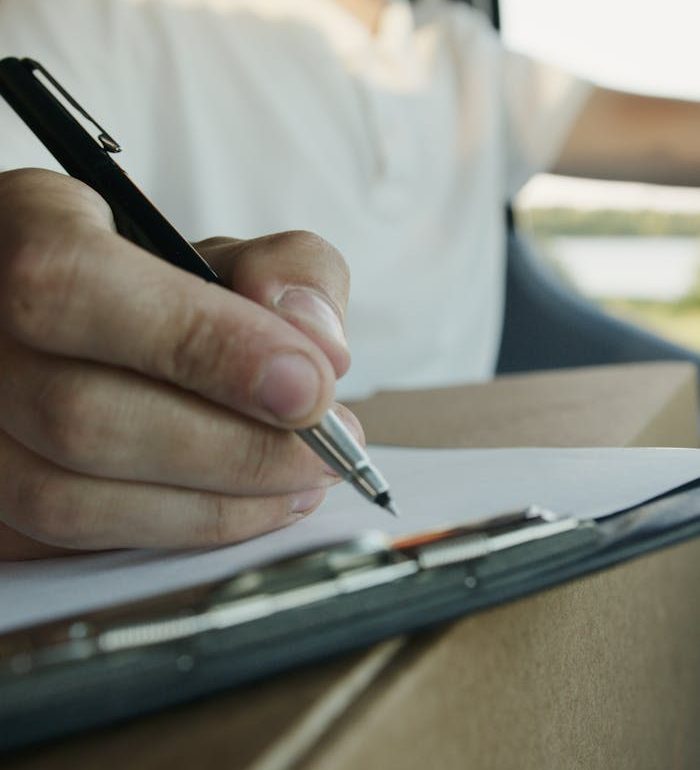 Close-up of a delivery driver writing on a clipboard while holding a package inside a vehicle.